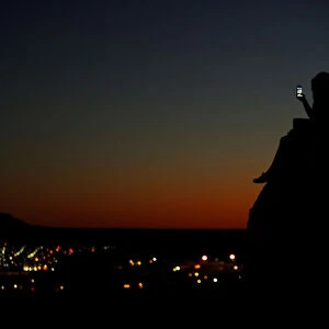 A young couple look at their phone as they sit on a hillside after sun set in El Paso