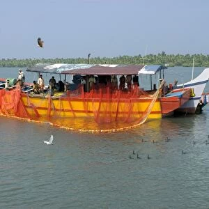Fishing boat with fishermen rolling back nets in brackish lagoon after day fishing at sea, Kollam, Alleppey Backwaters
