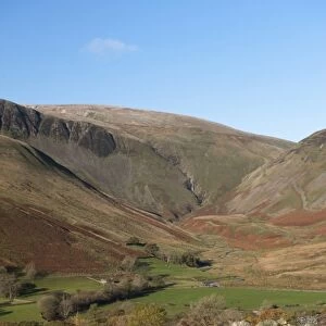 View of drystone wall and farmland in fell valley, with waterfall in distance