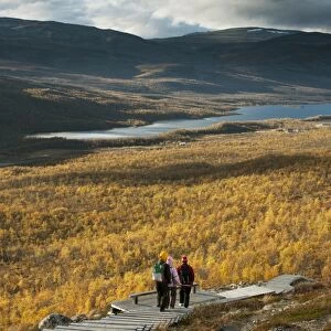 Walkers on boardwalk leading to summit of fell, Malla Strict Nature Reserve and Lake Kilpisjarvi in background
