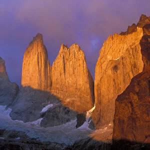 Clouds swirl around the sunrise-colored rocky points of Cerro del Torres in Patagonia