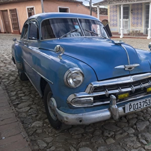 Cuba, Trinidad. Blue taxi parked on cobblestones