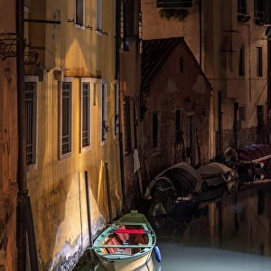 Europe, Italy, Venice. Wooden boat and reflections on still canal at night