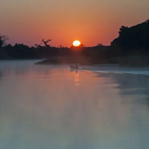 South America, The Pantanal, Brazil, A lone boat at sunrise driving through the rising