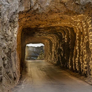 Tunnel on Iron Mountain Road lit by setting sun with view of Mount Rushmore near Keystone