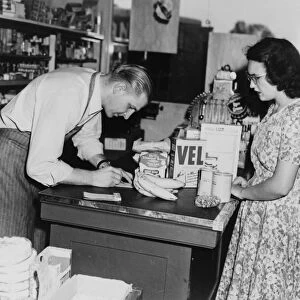 BANANA INDUSTRY, c1948. At a grocery store, a clerk writes up a customers grocery bill