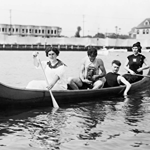 CANOE, c1910. Two women paddling a canoe with two men, one holding a camera. Photograph