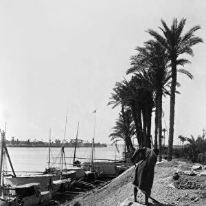 EGYPT: CAIRO. A view along the Nile with boats docked and a man shoveling on the shore