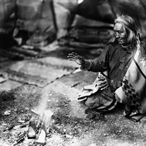 NAVAJO MAN, c1915. A Navajo man warming his hands over a fire in a tepee. Photograph by William Carpenter, c1915