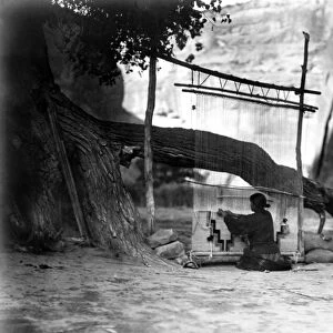 NAVAJO WEAVER, c1905. A Navajo woman weaving a blanket under a cottonwood tree, with a canyon wall in the background. Photograph by Edward Curtis, c1905