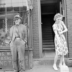 NYC: 14th STREET, 1942. A man and woman outside of a shop on 14th Street in New York City