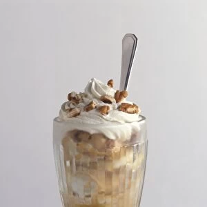 Banoffee glory, ice cream sundae made with bananas and toffee, topped with whipped cream and nuts, with spoon, close-up