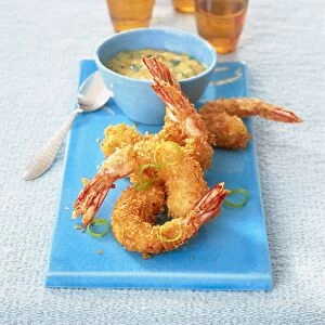 Battered prawns, bowl and spoon on a blue chopping board, orange glasses in background, elevated view