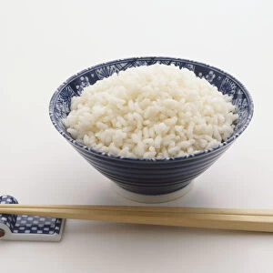 Bowl of rice with chopsticks lying next to it
