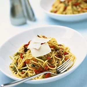 Bowl of spaghetti with chopped tomatoes, herbs and parmesan shavings, and a fork, close-up