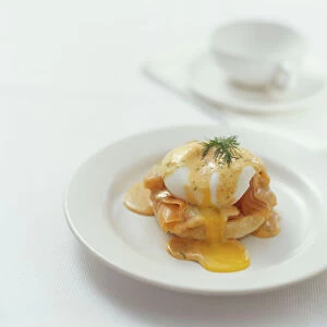 Eggs Benedict topped with salmon and hollandaise sauce, garnished with a sprig of dil
