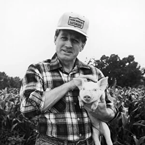 Farmer in field holding baby pig