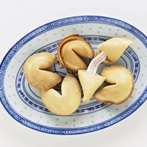 Fortune cookies on china tray, one of them broken in half with note revealed in the middle, view from abive