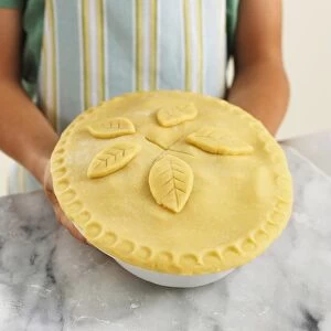 Girl holding apple pie with pastry lid in baking dish