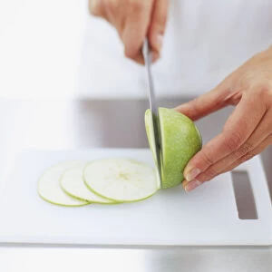 Green apple being thinly sliced on chopping board, front view