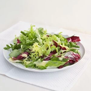 Green and red leaf salad on white plate with napkin on table