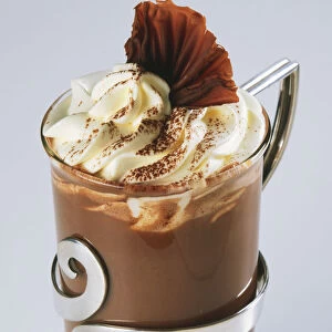 Hot Chocolate topped with whipped cream and chocolate curls in decorated glass, close up