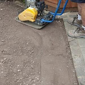 Man using soil compacter to flatten ground in garden near shed