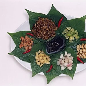 Miang Kham, a Thai snack dish of ginger, coconut, lemons, red onions, dried shrimps, peanuts and a syrup sauce, served on leaves, garnished with red chilli peppers