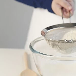 Person sieving flour into glass bowl