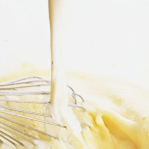 Poured milk being whisked into egg and sugar mixture, close-up