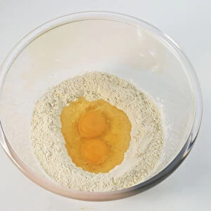 Two raw eggs in a well of flour inside glass bowl