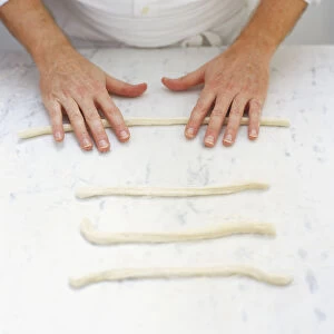 Rolling strips of dough back and forth on floured surface, high angle view