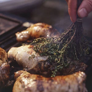 A tied bunch of herbs being used to baste chicken legs stuffed with mushrooms