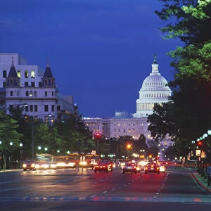 View of the tree-lined, commuter traffic-filled Pensylvania Avenue seen at night with the US Capitol building lit-up in the distance
