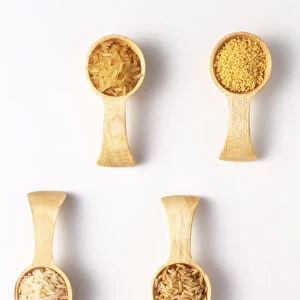 White long-grain rice, easy-cook rice, brown rice and couscous in wooden spoons