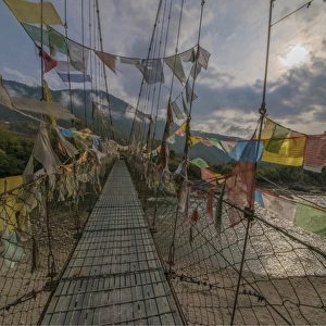 Prayer flags flutter in the breeze on a suspended footbridge over the Punakha river, Bhutan