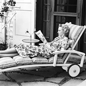 Blonde woman reading magazine on chaise lounge