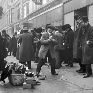 A crowd on a sidewalk observes street peddlers selling toys