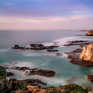 The dangerous and rugged coastline of Arniston where many shipwrecks have taken place with sunrise painting the cliff face and clouds with color. Arniston, Western Cape Province, South Africa