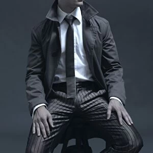 Fashion shot of a man in a suit and jacket, sitting on a stool