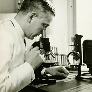 Male doctor using microscope in surgery, (B&W)