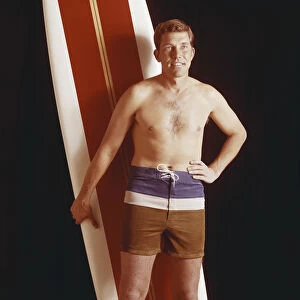 Mid adult man holding surfboard against black background