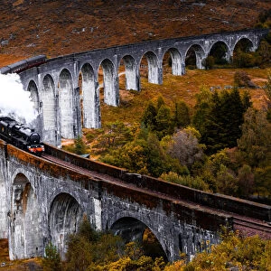 Steam train crossing the Glenfinnan bridge with autumn colors in Scotland