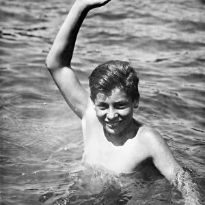 Teenage boy (16-17) standing deep in water, waving, (B&W), portrait