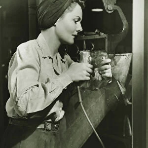 Woman working with electric drill in factory, (B&W)
