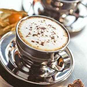 Stainless steel cup of cappucino on metal counter with chocolate fudge and pthysalis