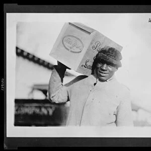 African American man carrying a case of "Four Roses"whiskey on his shoulder