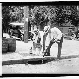 Two men pouring liquor into storm drain, 8 July 1921 (b / w photo)