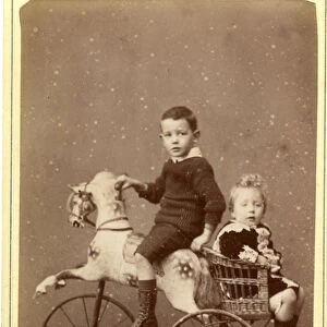 Young boy on rocking horse with young girl in wicker carriage behind