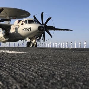 An E-2C Hawkeye sits on the flight deck of USS Abraham Lincoln while sailors man